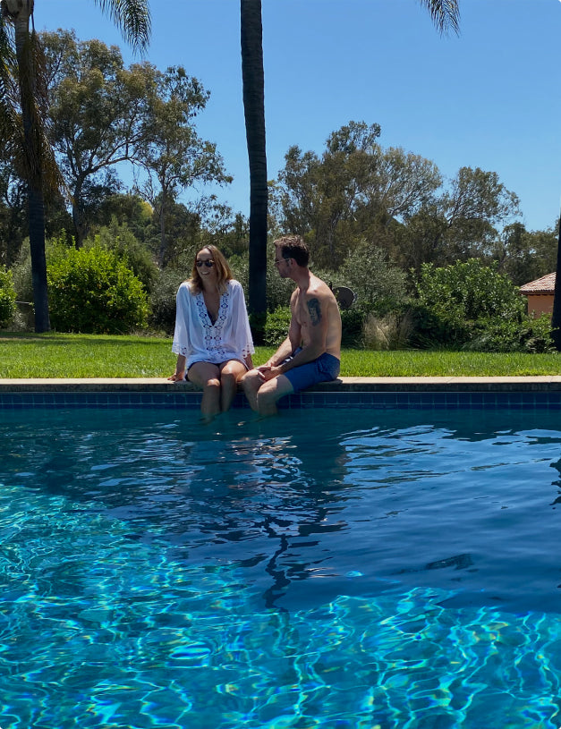 two people sitting on the edge of a pool